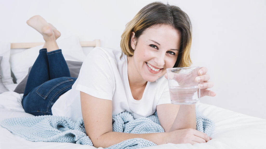 Girl smiling in bed while drinking water from her morning routine checklist